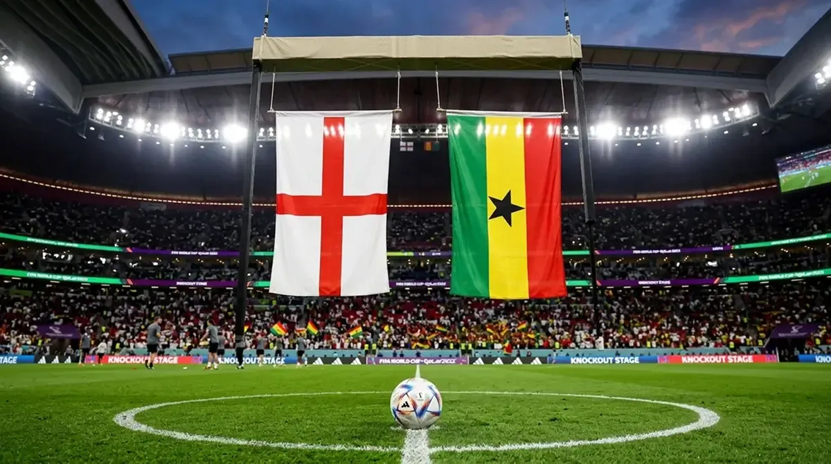 England and Ghana national team flags beside a World Cup match ball under stadium floodlights