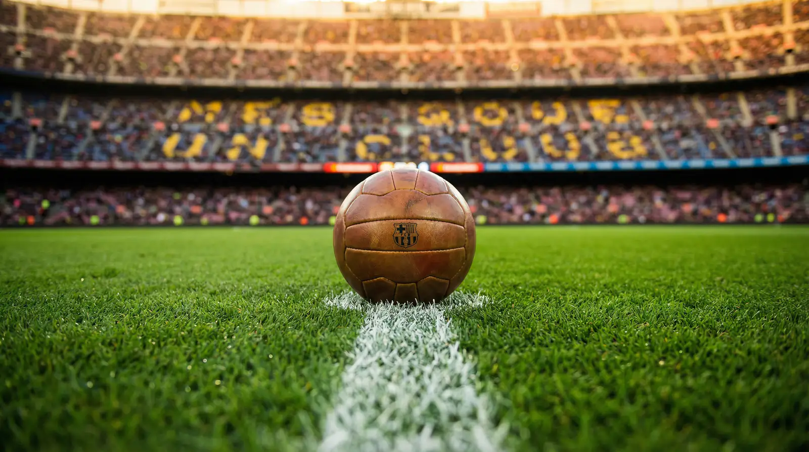 Close-up of a football resting on the centre circle of a freshly cut pitch inside a full stadium before kick-off