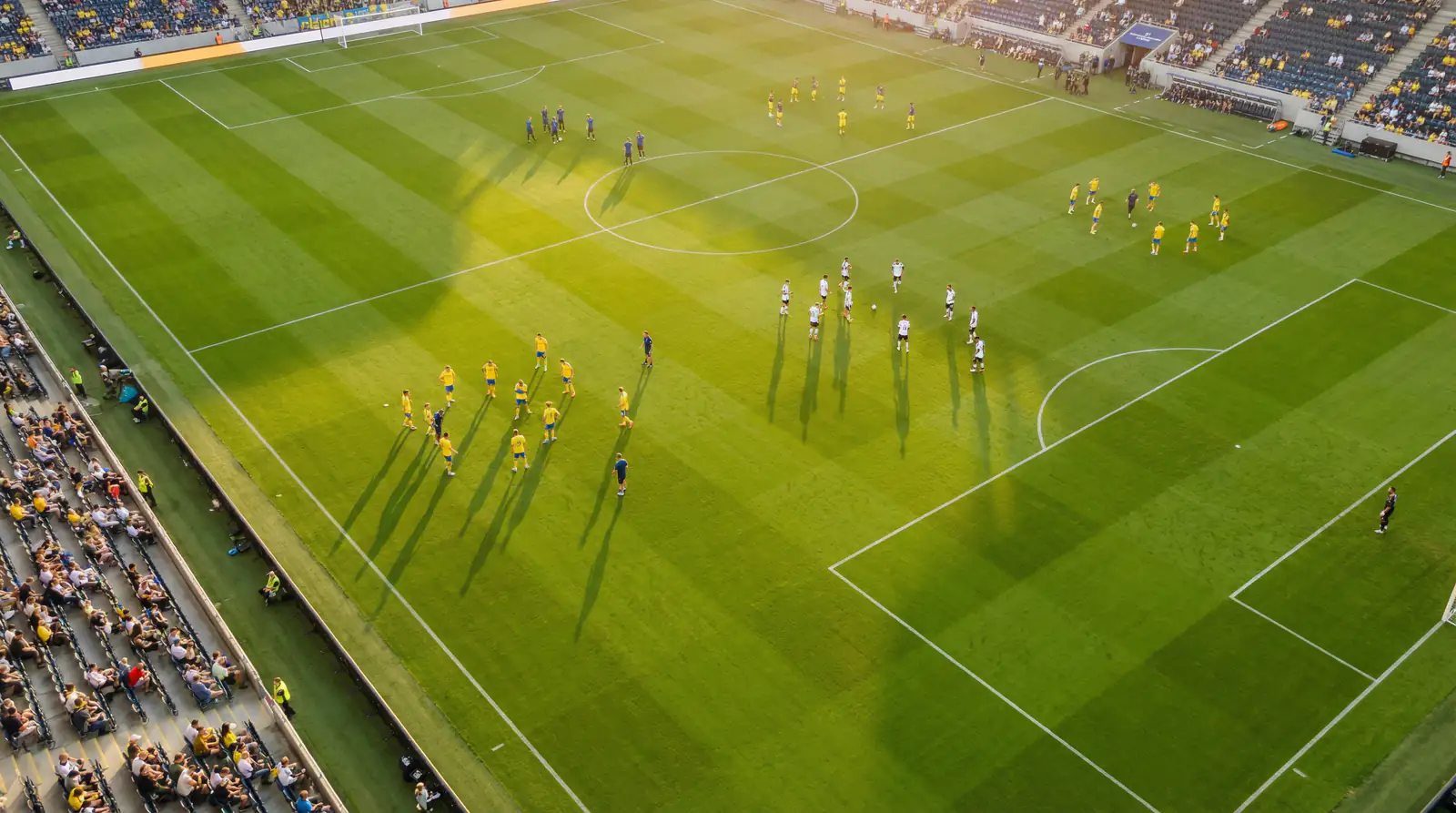 Aerial view of a modern football pitch with players from multiple nations warming up before a World Cup group match