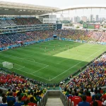 Wide-angle view of a World Cup stadium during a group stage match with full stands and pitch markings visible