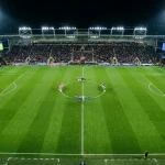 Aerial view of a professional football pitch with players positioned for kick-off under floodlights