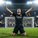 Football striker celebrating after scoring a goal with arms raised inside a full stadium